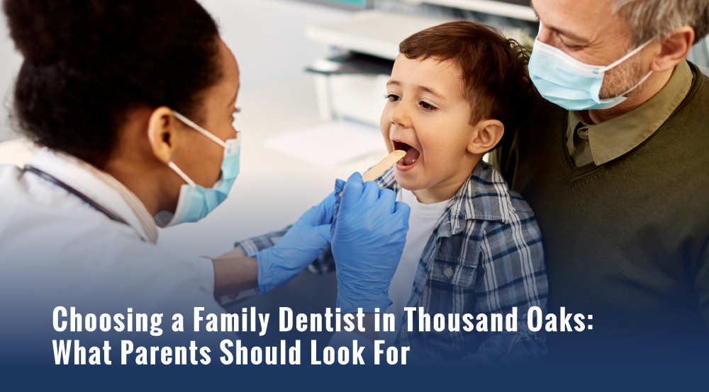 Family dentist examining a young boy's mouth with a tongue depressor as an older man holds him